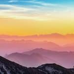 Sunrise over layered mountain silhouettes with a blue-to-orange gradient sky. **