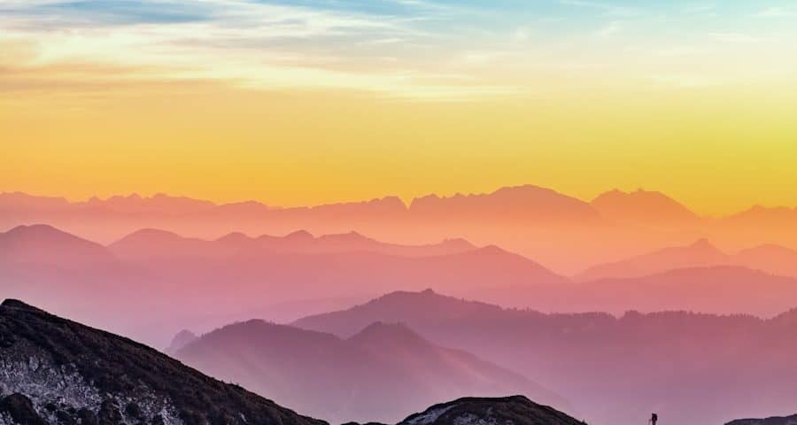 Sunrise over layered mountain silhouettes with a blue-to-orange gradient sky. **