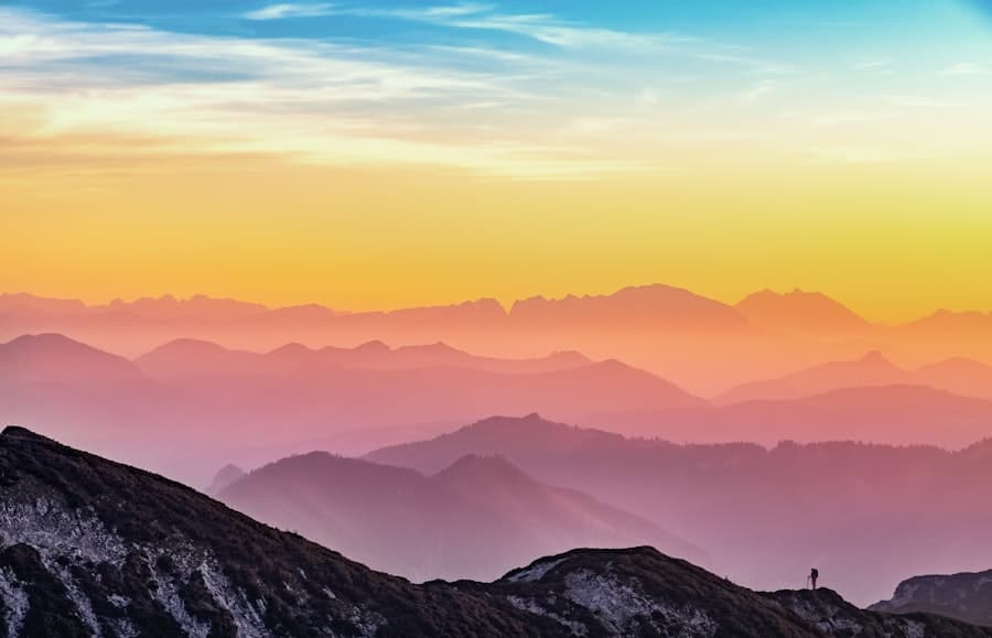 Sunrise over layered mountain silhouettes with a blue-to-orange gradient sky. **